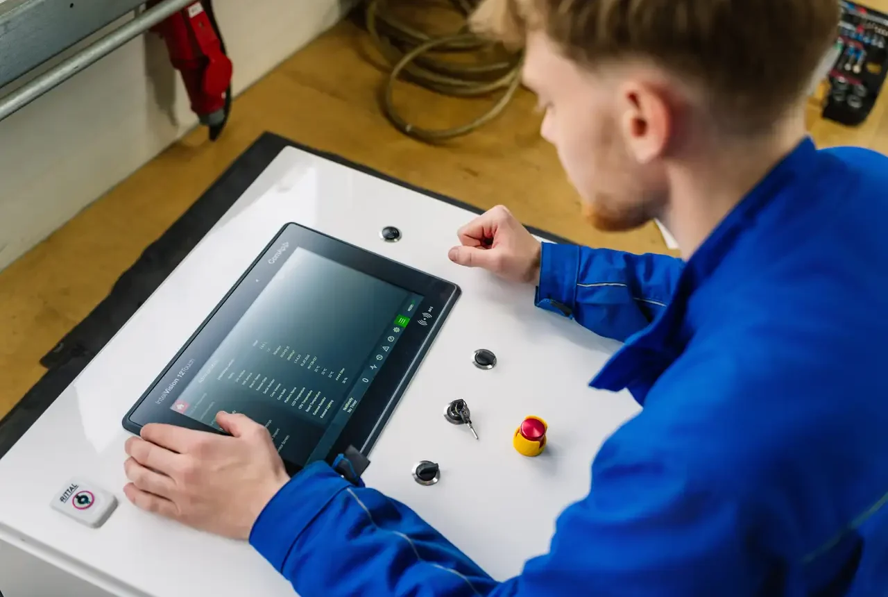 Techniker in blauer Arbeitskleidung bedient ein Kontrollpanel mit Touchscreen in einem Prüffeld.