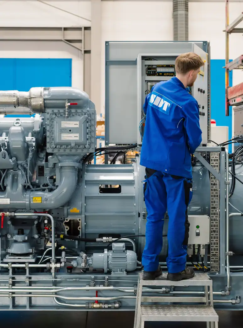 Techniker in blauer Arbeitskleidung arbeitet an einer großen Industriemaschine in einer Fabrikhalle.