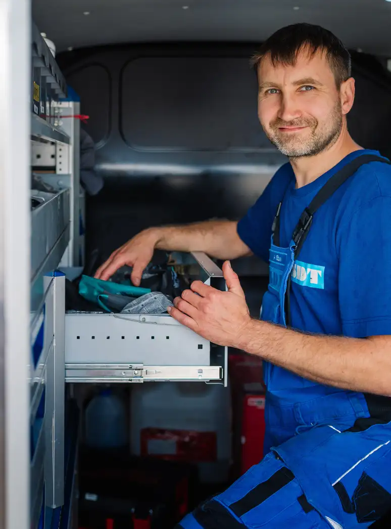 Handwerker in blauer Arbeitskleidung sortiert Werkzeuge in einem Lieferwagen.