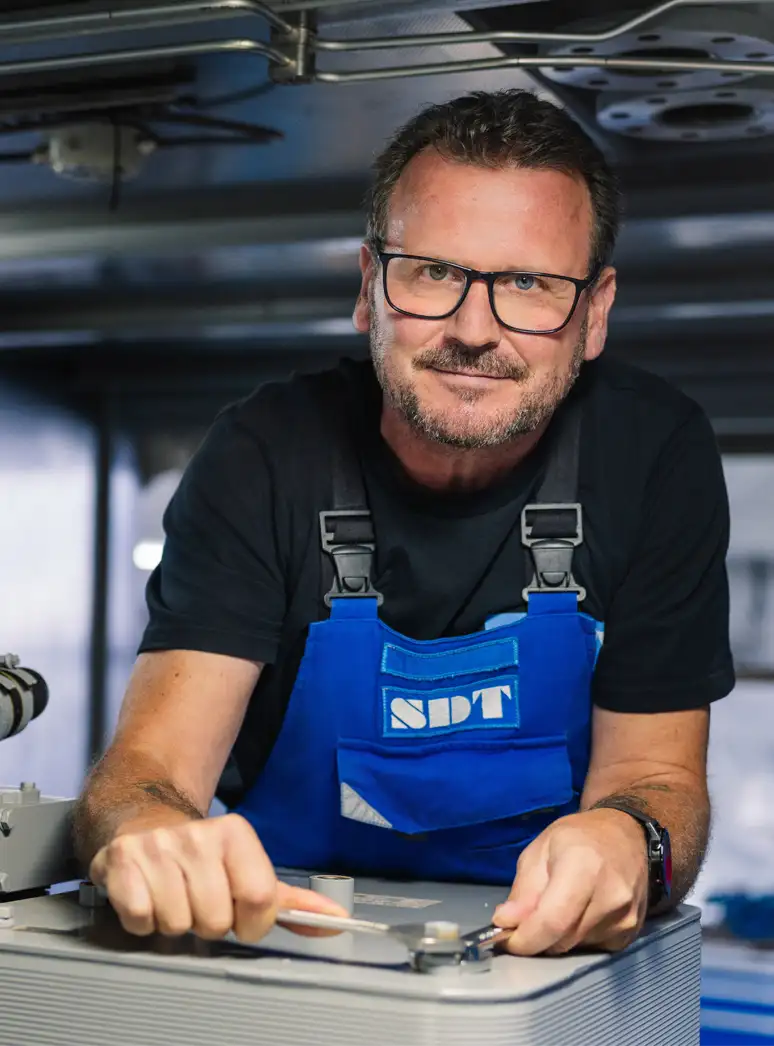 Mann in blauer Arbeitskleidung arbeitet mit Werkzeug an einer Maschine.