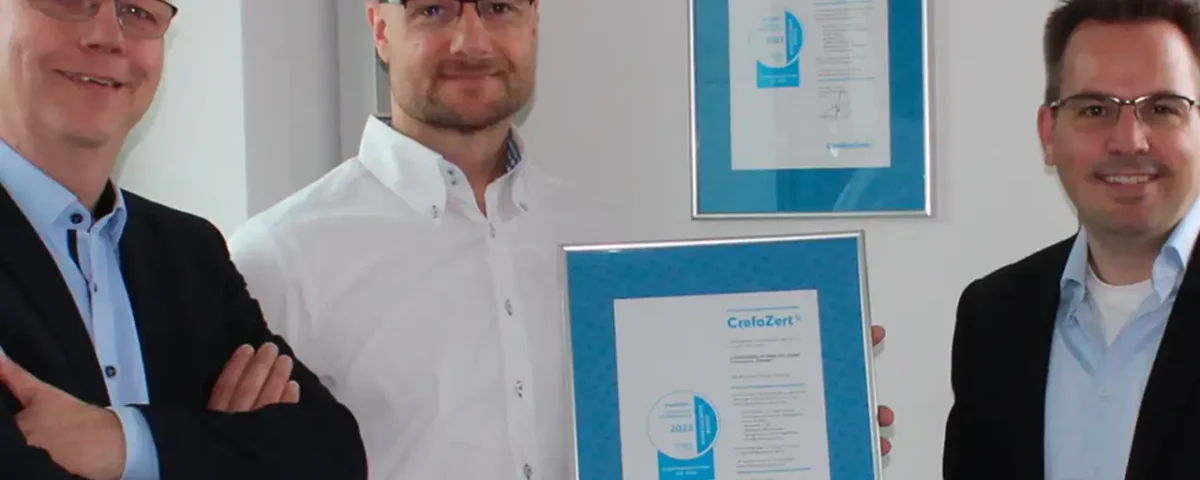 Drei Männer präsentieren stolz das CrefoZert Bonitätszertifikat, das sie im zweiten Jahr in Folge erhalten haben.
