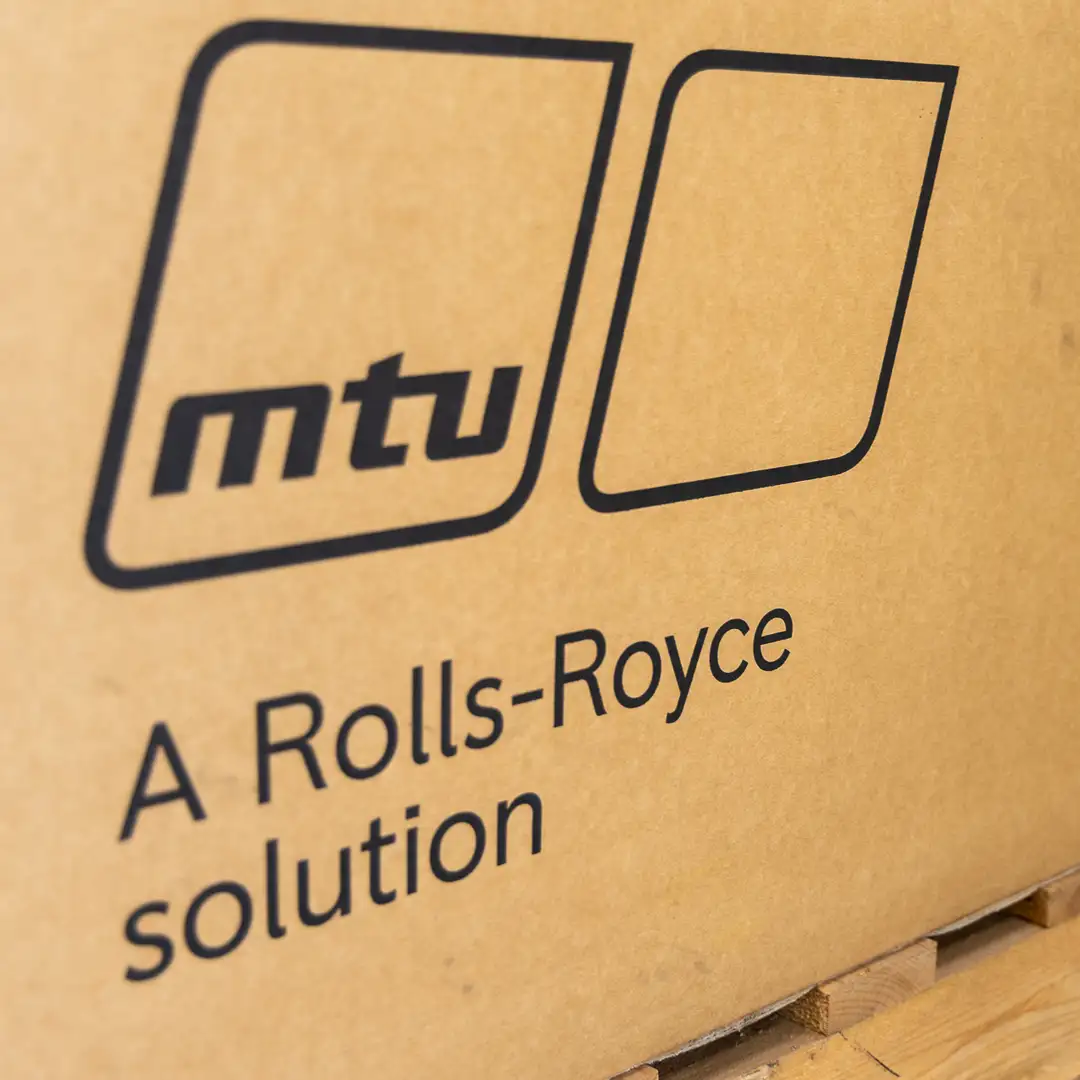 Karton mit dem Logo von MTU und dem Schriftzug "A Rolls-Royce solution" auf einer Palette.