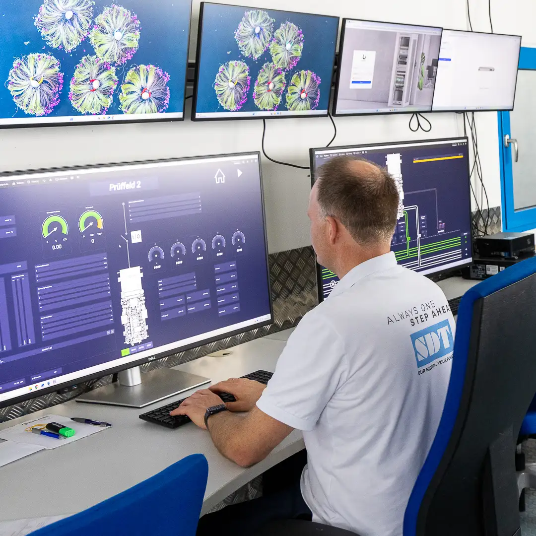 Mann überwacht technische Daten auf mehreren Bildschirmen in einem Kontrollraum.