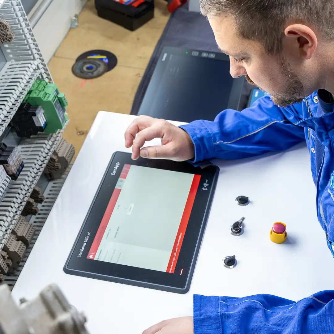 Techniker in blauer Kleidung arbeitet mit einem Tablet in einer Werkstattumgebung.