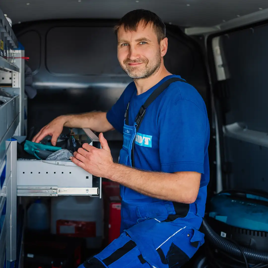 Handwerker in blauer Arbeitskleidung arbeitet im Inneren eines Lieferwagens und sortiert Werkzeuge in einer Schublade.