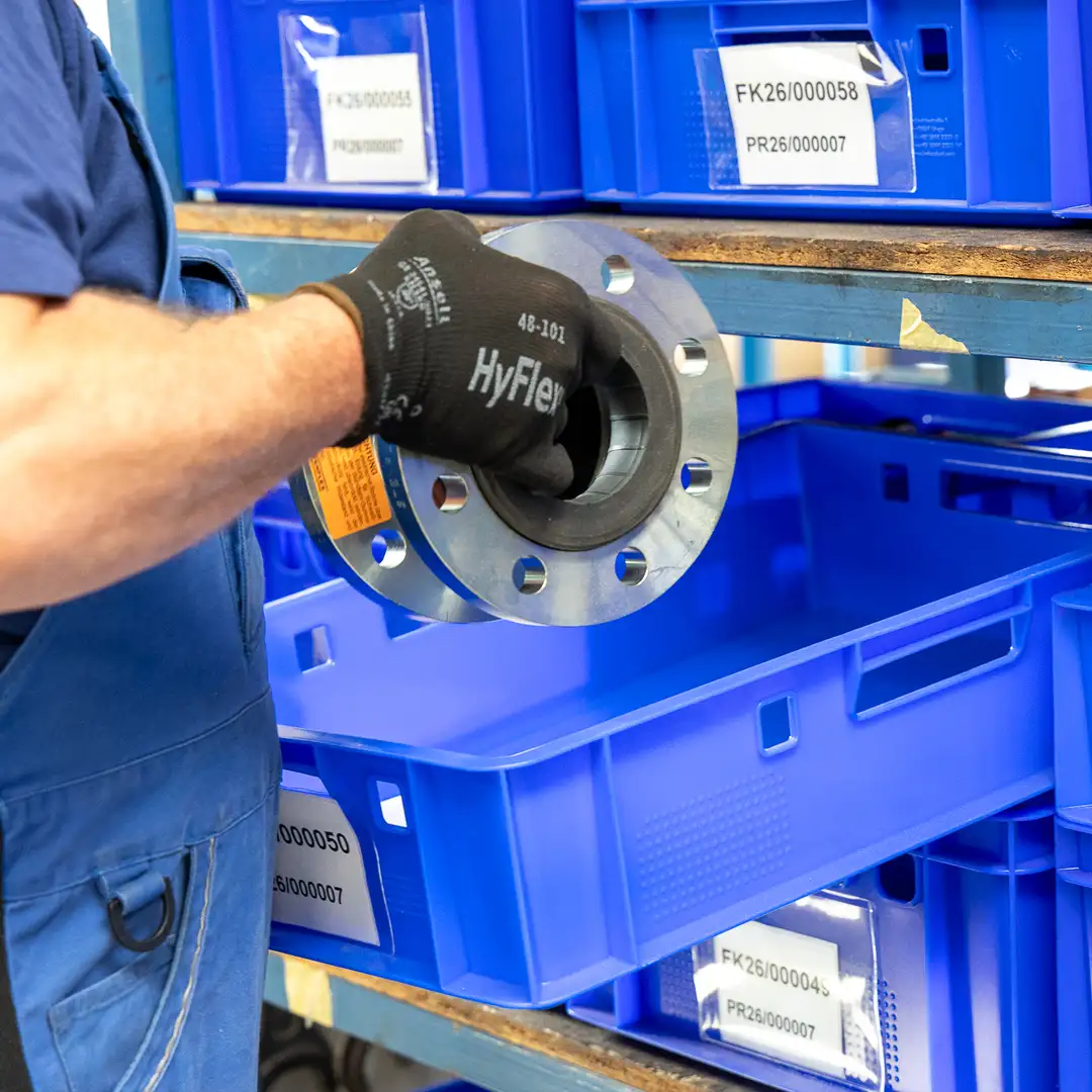Mitarbeiter lagert metallene Flanschkomponente in blaue Kunststoffkisten im Lager.