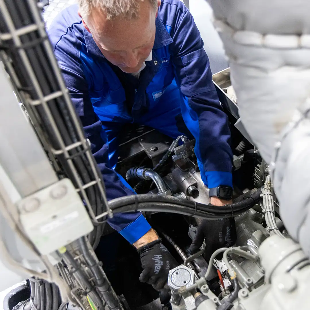 Techniker in blauer Arbeitskleidung führt Wartungsarbeiten an einer komplexen Maschinenanlage durch.