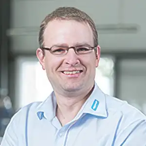 Lächelnder Mann mit Brille und blauem Hemd in einem Büro.
