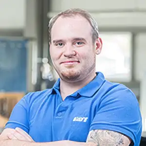 Mann in blauem Poloshirt mit verschränkten Armen steht in einem modernen Büro.