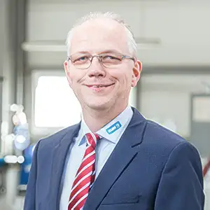 Mann in Anzug mit roter Krawatte lächelt in einer professionellen Umgebung.