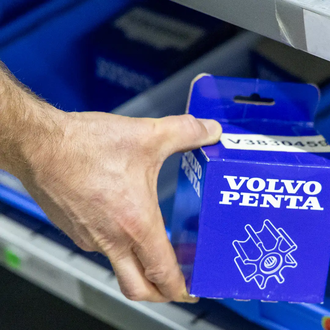 Hand greift nach einer blauen Volvo Penta Verpackung in einem Regal.