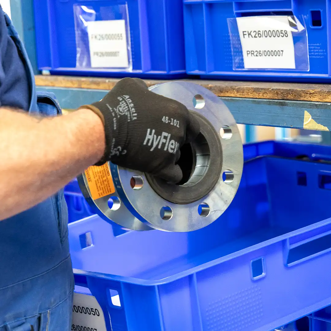 Arbeiter legt ein Metallteil in eine blaue Kiste im Lagerregal.
