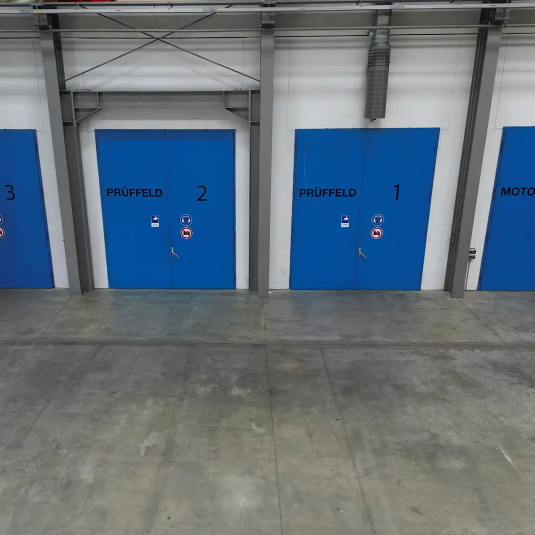 Blaue Türen eines Prüfbereichs in einer Industriehalle mit den Nummern 1, 2 und 3 auf grauem Boden.