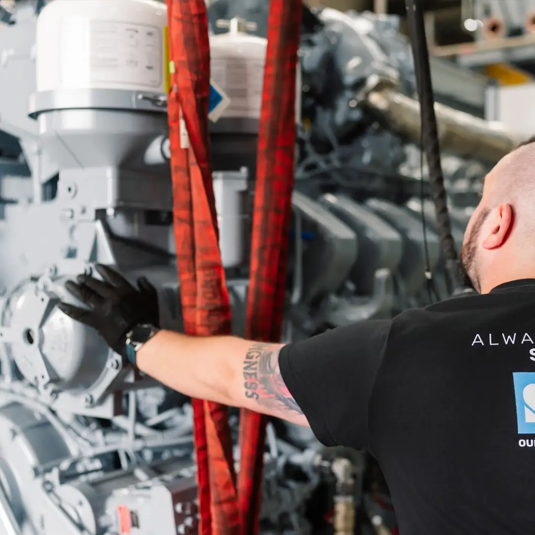 Mann in schwarzem T-Shirt arbeitet an einer großen Industriemaschine, umgeben von roten Hebebändern.
